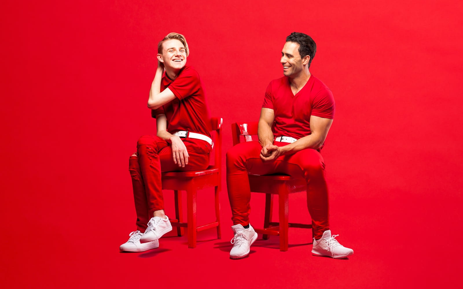 Become the One promotional image for Showcase Victoria. Two smiling people sit on red chairs, in front of a red backdrop. They are wearing red t-shirts and red pants with white belt and shoes.
